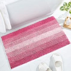 a bathroom rug with pink stripes on it next to slippers and a bathtub