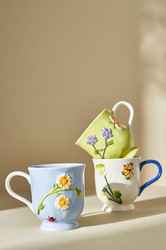 three coffee cups sitting on top of a counter next to each other with flowers painted on them