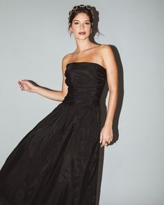 a woman in a strapless black dress poses for the camera with her hand on her hip