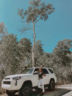 a woman standing next to a white toyota suv in front of a tree on a sunny day