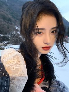 a woman with long black hair wearing a white lace top and red lipstick standing in the snow