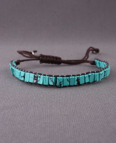 a bracelet with turquoise beads and leather cord on a gray background, it is made out of