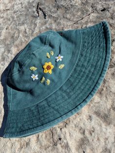 a green hat with yellow and white flowers on it sitting on top of some rocks