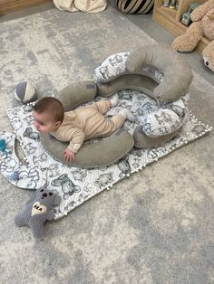 a baby laying on top of a rug next to a stuffed animal