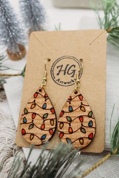 a pair of wooden earrings sitting on top of a card next to some pine branches