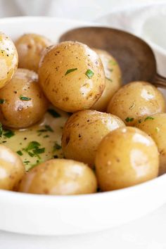 a white bowl filled with cooked potatoes and garnished with parsley on top