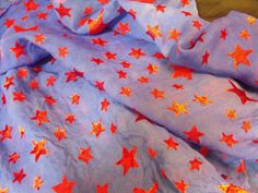 a purple and red star print fabric with orange stars all over it, on top of a bed