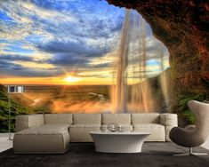 a living room with a couch, table and waterfall in the background at sunset or sunrise