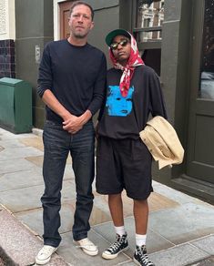 two men standing next to each other on a sidewalk