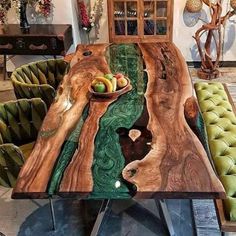 the table is made out of wood and has green velvet chairs around it, along with a bowl of fruit on top