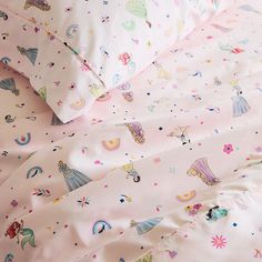 a pink bed with princess themed sheets and pillow cases on top of it, in front of a white background