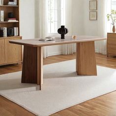 a wooden table sitting on top of a white rug in front of a book shelf