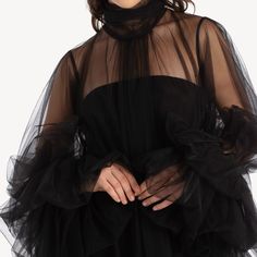 a woman wearing a black dress with sheer sleeves and ruffles on the bottom