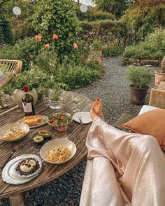 a woman sitting at a table with food and wine in front of her, looking out onto the garden