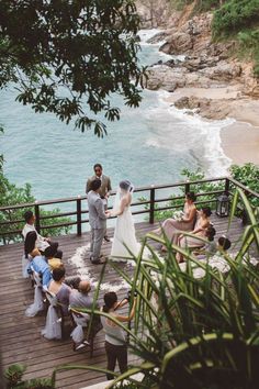 a group of people standing on top of a wooden deck next to the ocean and trees