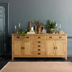 a wooden dresser with plants and candles on it in front of a gray wall, next to a rug