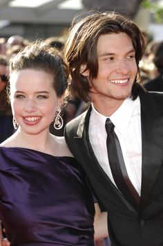 two people standing next to each other on a red carpet at an awards event with one person wearing a black suit and the other in a purple dress