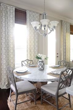 a dining room table with chairs and a vase on top of it in front of the window