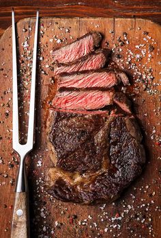 a steak on a cutting board next to a knife and fork