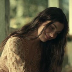 a woman is sitting down and smiling at the camera with her hair blowing in the wind