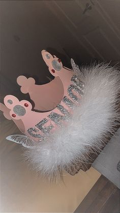 a pink tiara hanging from the ceiling with white feathers and silver decorations on it