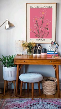 a wooden desk topped with a plant next to a white chair and a painting on the wall