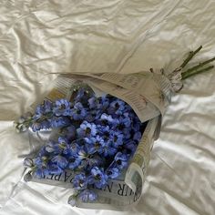 a bouquet of blue flowers is wrapped in plastic on a white sheeted bed spread