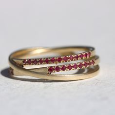 This beautiful criss cross ring is a stunning addition to any jewelry collection, especially for those born in the month of July as Ruby is their birthstone. Crafted from 14k yellow solid gold, it features three bands intertwined in a unique crossover design. The two outer bands are adorned with natural Ruby gemstones in a half eternity pave setting, while the center band is left unadorned for a simple and elegant touch. The 32 round cut Ruby gemstones have a brilliant shine that catches the light with every movement, making this dainty ruby ring a true statement piece. Rubies are known for their deep red color and are said to symbolize passion, love, and prosperity. The half eternity design symbolizes the eternal bond between loved ones, making this ring a perfect choice for a meaningful Yellow Gold 14k Eternity Band With Birthstone, 14k Yellow Gold Eternity Band With Birthstone, Yellow Gold Eternity Band With Birthstone For Anniversary, Gold Eternity Band With Birthstone, 14k Gold Eternity Band With Birthstone For Anniversary, Yellow Gold Eternity Band With Birthstone For Promise, Promise Ring Eternity Band With Birthstone In Yellow Gold, Dainty Ruby Ring, Ruby Eternity Band