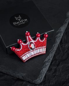 a red crown brooch sitting on top of a black box