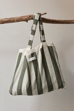 a green and white striped bag hanging from a wooden hanger on a wall next to a branch