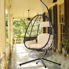 a hanging chair on the front porch with white pillows and black stand alone swinger