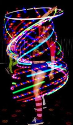 a woman standing in front of a hula hoop with colorful lights on her body