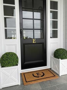 the front door is decorated with two white planters and a monogrammed door mat