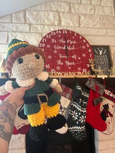 a person holding a knitted teddy bear in front of a fireplace with stockings on it