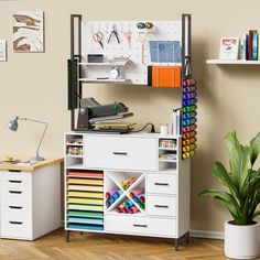 a white desk with lots of crafting supplies on top of it and a potted plant in the corner