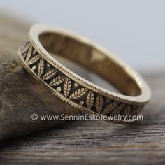 a wedding band with leaves on it sitting on top of a wooden table next to a rock