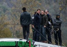 several people standing on top of a boat in the water with trees behind them and one person holding a camera