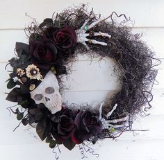 a wreath decorated with fake flowers and skulls is displayed on a white wooden wall,