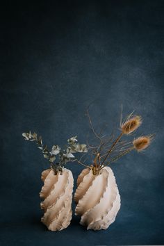 two vases with dried flowers in them on a blue tableclothed surface, against a dark background