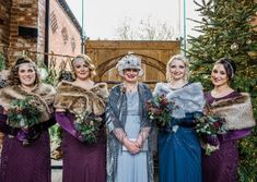 four women in long dresses and fur stoles posing for the camera with christmas trees behind them