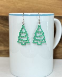 two green christmas tree shaped earrings sitting on top of a white cup