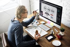 a man sitting at a desk drawing on a computer screen with markers and pencils