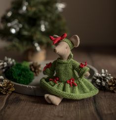 a stuffed mouse in a green dress sitting on a plate next to pine cones and a christmas tree