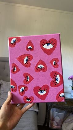 a hand holding up a pink box with hearts and eyes painted on it