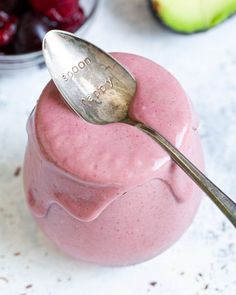 a spoon sticking out of a pink smoothie in a bowl with cherries on the side