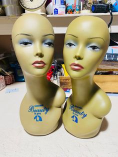 two mannequin heads sitting next to each other in front of a clock on a table