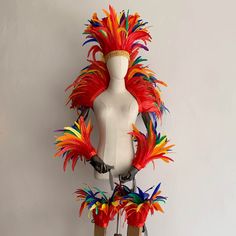 a white mannequin with colorful feathers on it's head and legs in front of a white wall