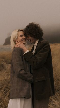 a man and woman standing next to each other in front of some tall brown grass