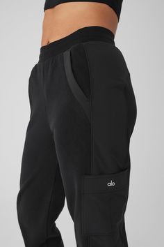 the back view of a woman wearing black sweatpants with pockets on both sides and white logo