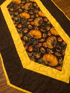 a black and yellow quilted table runner with pumpkins on the border, sitting on a wooden surface